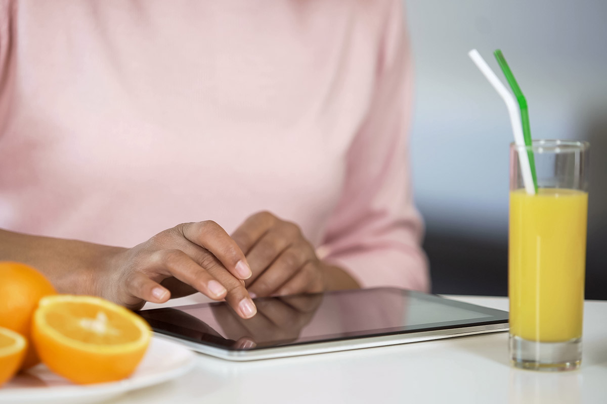 Girl typing on tablet, oranges and fresh juice on table, blogging about dieting