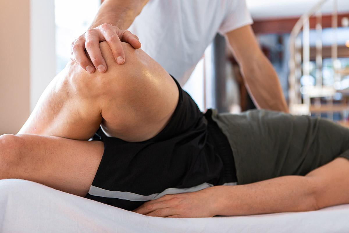 A sportsman receiving medical massage of legs. A young man lying on the massage table and having a treating leg massage in the medical center